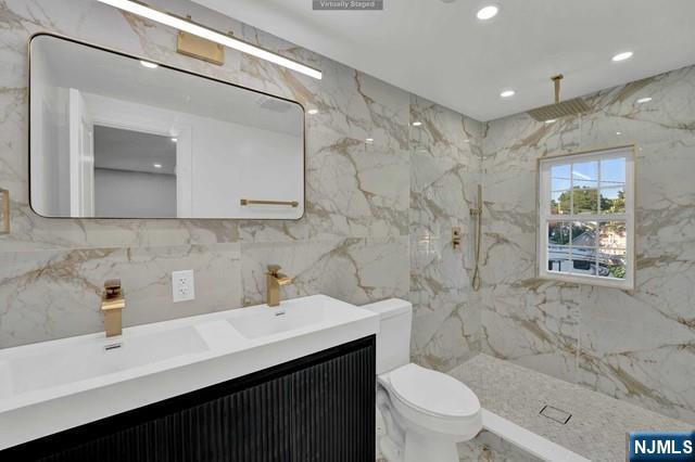 bathroom with vanity, toilet, tile walls, and a tile shower