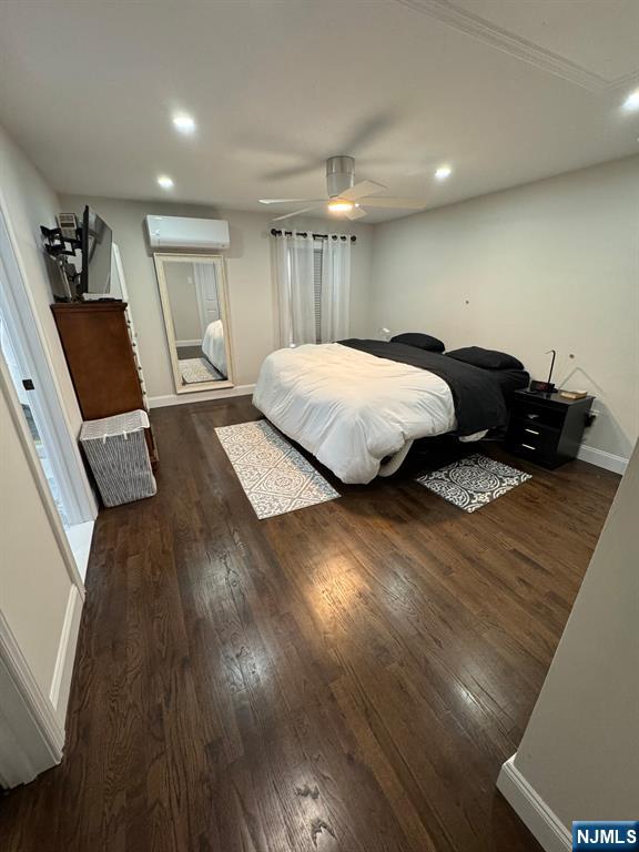 bedroom with ceiling fan, dark hardwood / wood-style floors, and a wall unit AC