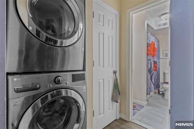 clothes washing area with light wood-type flooring and stacked washing maching and dryer