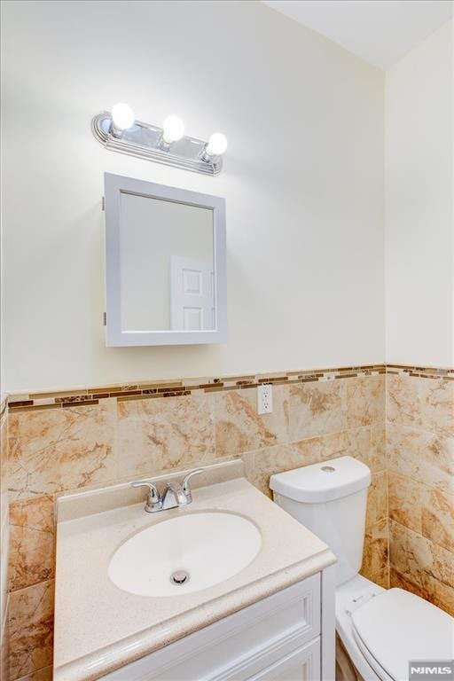 bathroom featuring vanity, toilet, and tile walls