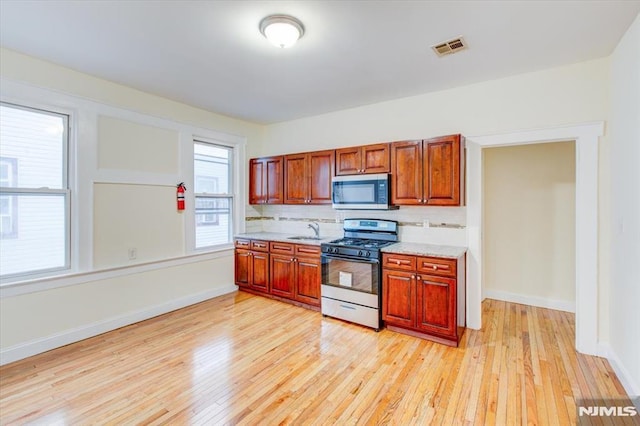 kitchen with sink, light hardwood / wood-style flooring, decorative backsplash, light stone counters, and stainless steel appliances