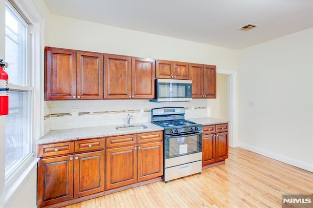 kitchen featuring sink, decorative backsplash, light stone countertops, light wood-type flooring, and stainless steel appliances