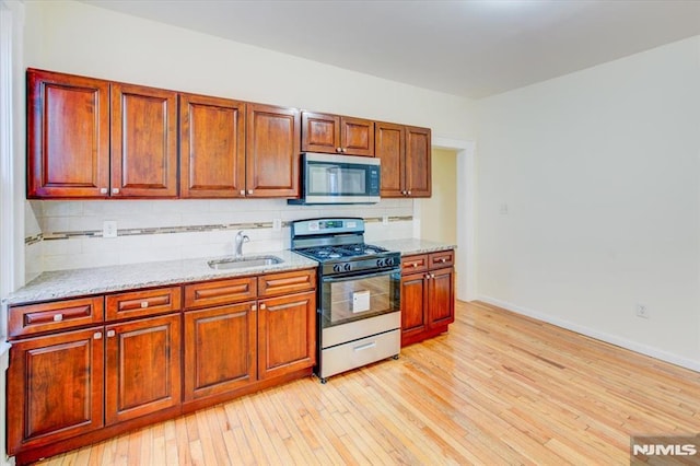 kitchen featuring decorative backsplash, light stone countertops, sink, and appliances with stainless steel finishes