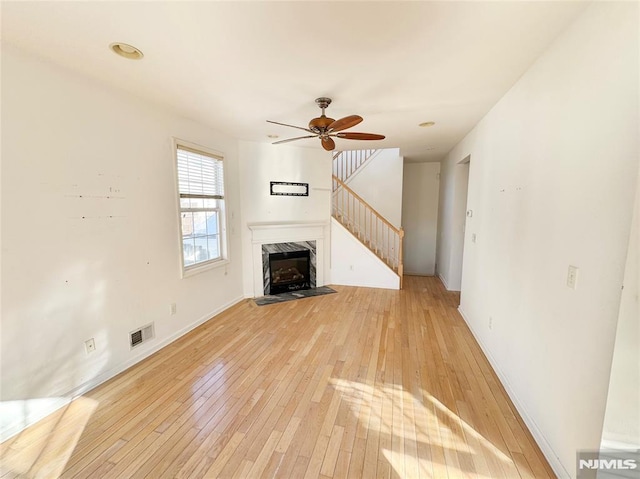 unfurnished living room with a premium fireplace, ceiling fan, and light wood-type flooring