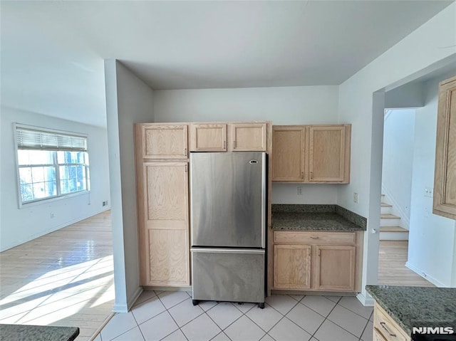 kitchen with stainless steel fridge, light tile patterned floors, light brown cabinets, and dark stone counters