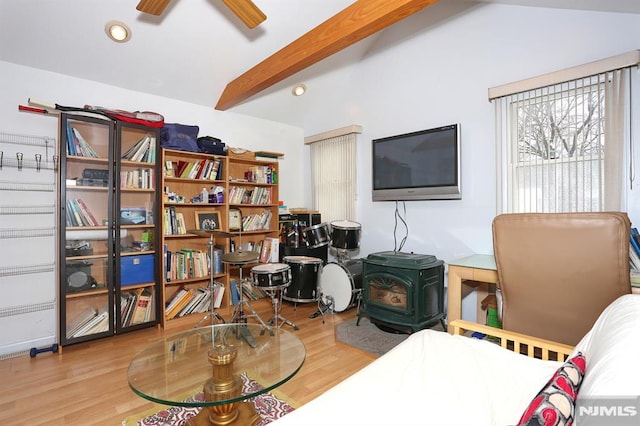 living area with ceiling fan, a wood stove, hardwood / wood-style floors, and lofted ceiling with beams