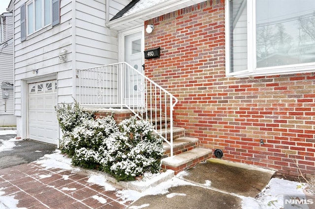 snow covered property entrance with a garage