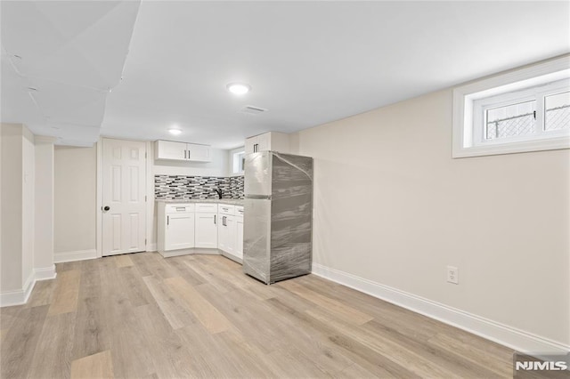 kitchen featuring white cabinetry, sink, light hardwood / wood-style flooring, backsplash, and stainless steel fridge