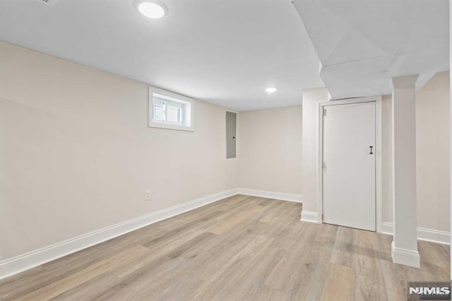 basement featuring electric panel and light hardwood / wood-style flooring