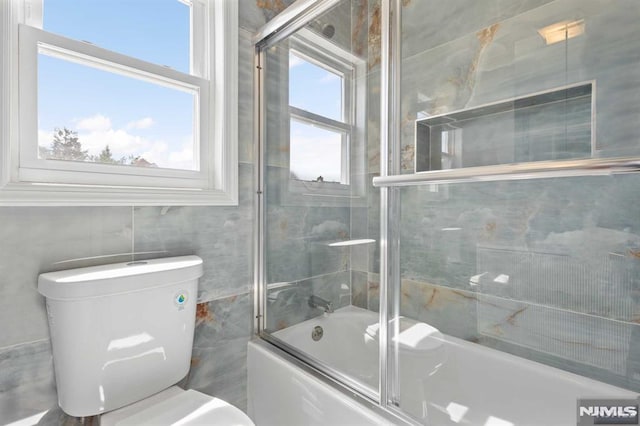 bathroom featuring toilet, plenty of natural light, and combined bath / shower with glass door