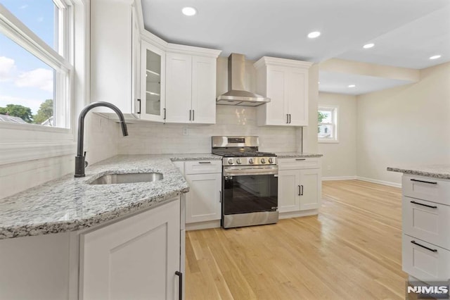 kitchen with sink, wall chimney range hood, stainless steel range oven, decorative backsplash, and white cabinets