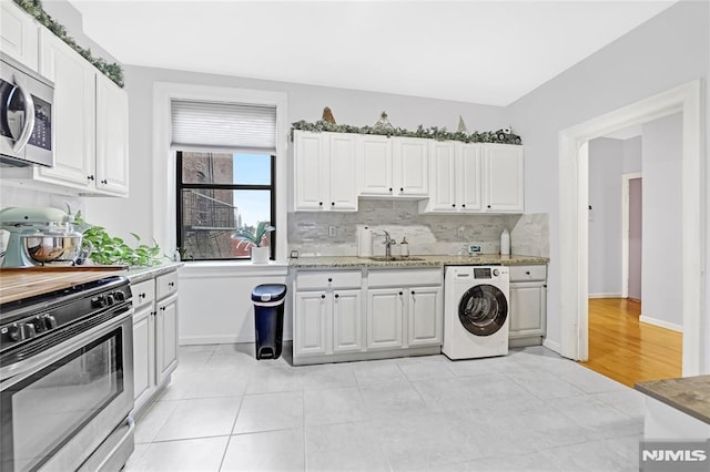 kitchen featuring appliances with stainless steel finishes, sink, light tile patterned floors, washer / dryer, and white cabinetry