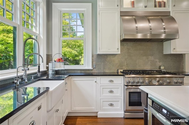 kitchen with decorative backsplash, high end stove, sink, wall chimney range hood, and white cabinets