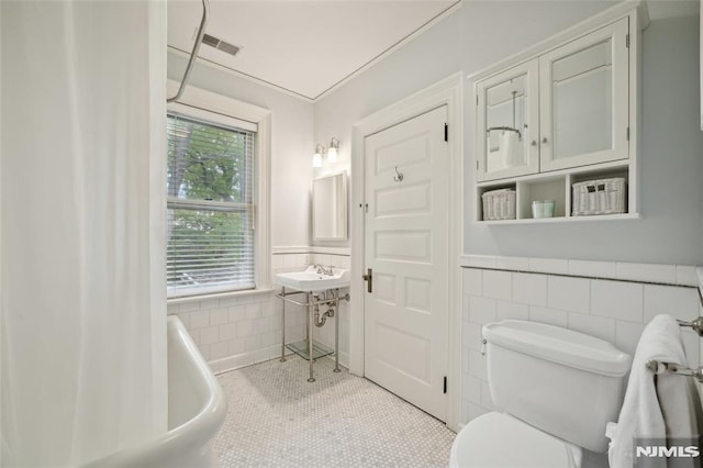 bathroom with a washtub, tile patterned flooring, tile walls, and toilet