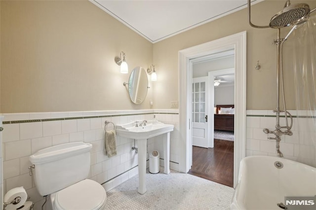 bathroom with a bathtub, tile patterned flooring, toilet, ornamental molding, and tile walls