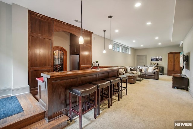 bar featuring stainless steel fridge, light colored carpet, and hanging light fixtures