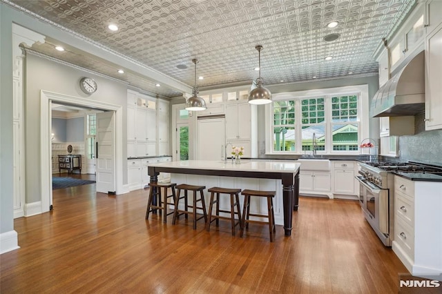 kitchen featuring high quality appliances, white cabinets, sink, an island with sink, and decorative light fixtures