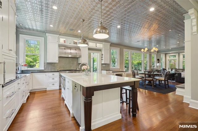 kitchen with white cabinetry, an island with sink, hanging light fixtures, and wall chimney range hood