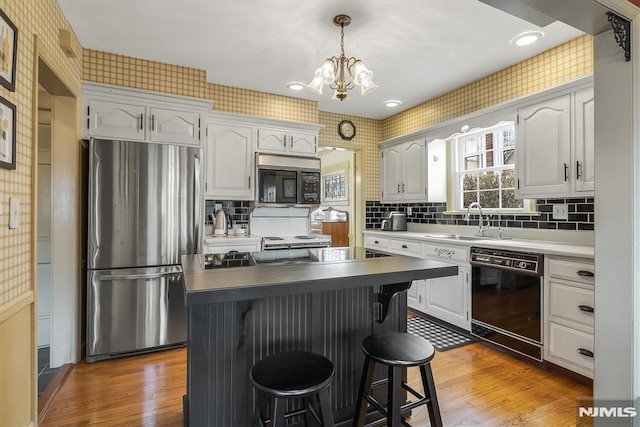 kitchen featuring sink, a breakfast bar, black appliances, and white cabinetry