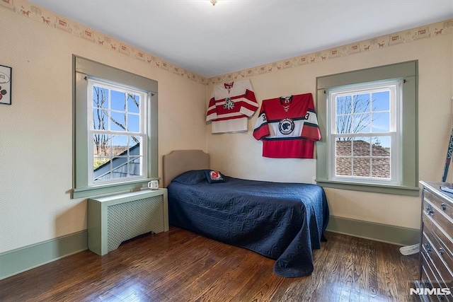 bedroom with radiator heating unit, multiple windows, and dark hardwood / wood-style floors