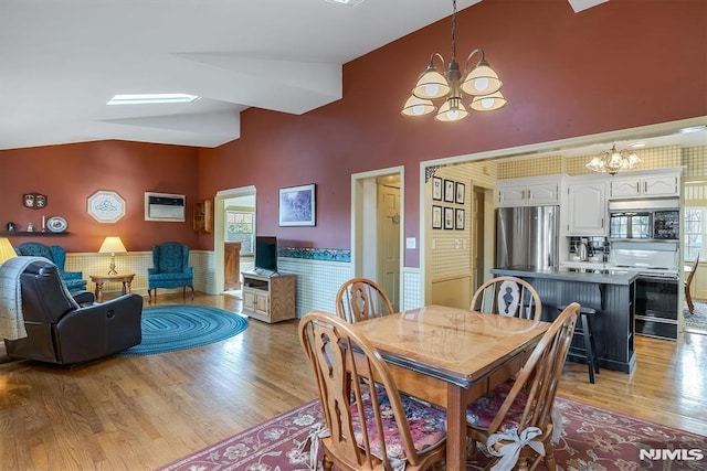 dining space with a wall mounted AC, vaulted ceiling with skylight, a notable chandelier, and light hardwood / wood-style flooring