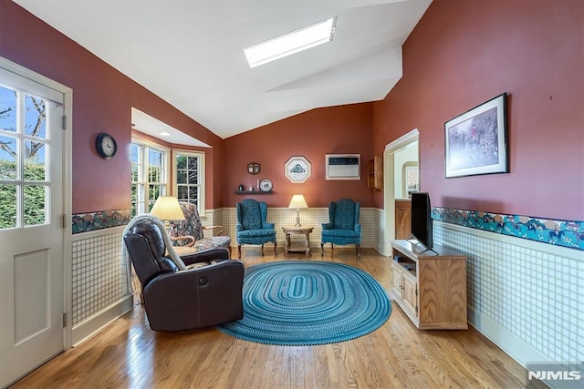 sitting room featuring vaulted ceiling with skylight and light hardwood / wood-style flooring