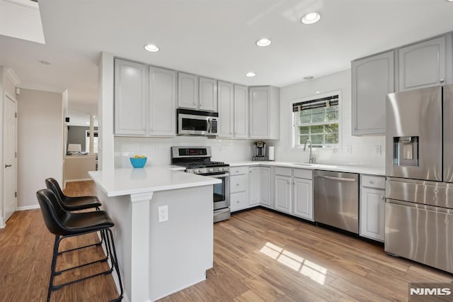 kitchen featuring appliances with stainless steel finishes, kitchen peninsula, a breakfast bar, decorative backsplash, and sink