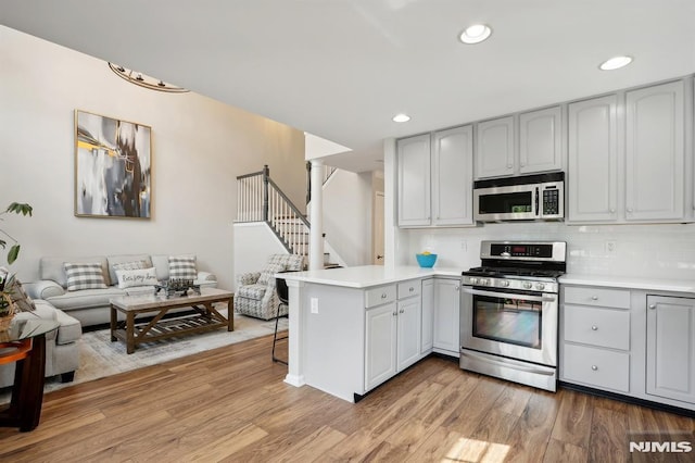 kitchen with stainless steel appliances, light hardwood / wood-style floors, gray cabinetry, and kitchen peninsula