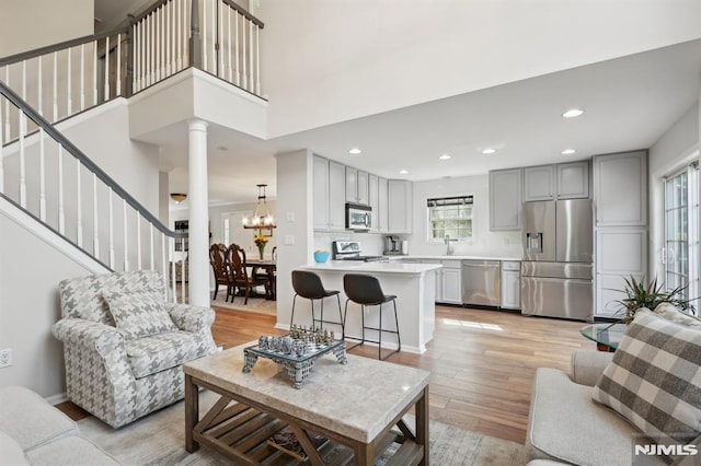 living room featuring a high ceiling, decorative columns, light wood-type flooring, and an inviting chandelier