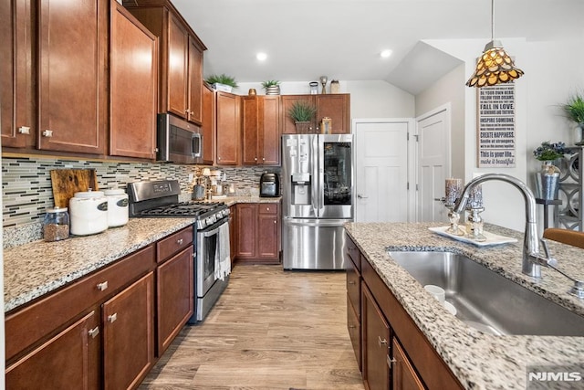 kitchen with sink, hanging light fixtures, light wood-type flooring, light stone counters, and stainless steel appliances