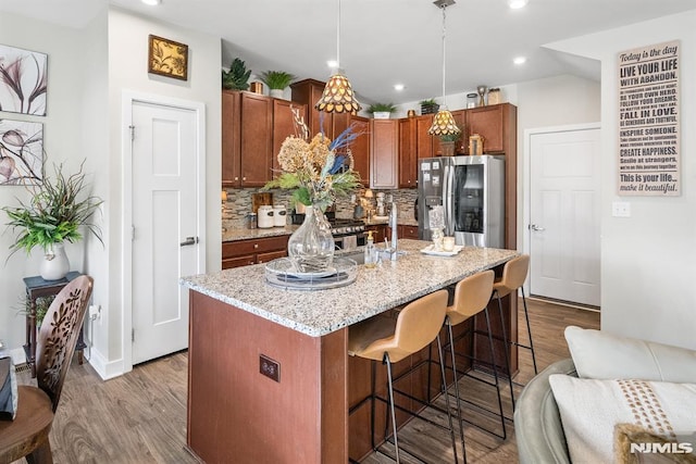 kitchen with pendant lighting, stainless steel refrigerator with ice dispenser, an island with sink, tasteful backsplash, and a kitchen bar