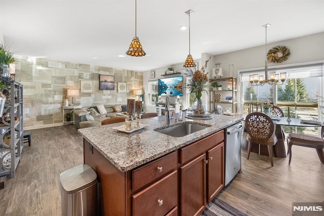 kitchen with light stone countertops, dishwasher, a chandelier, pendant lighting, and a kitchen island with sink