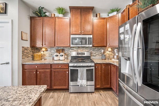 kitchen featuring stainless steel appliances, light stone counters, tasteful backsplash, and light hardwood / wood-style floors