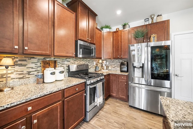 kitchen with decorative backsplash, light stone counters, stainless steel appliances, and light hardwood / wood-style floors