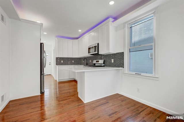 kitchen with kitchen peninsula, appliances with stainless steel finishes, white cabinetry, and a kitchen bar