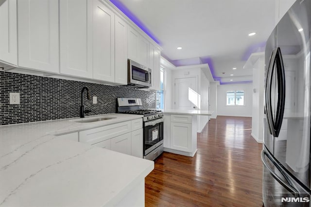 kitchen with stainless steel appliances, tasteful backsplash, light stone countertops, white cabinets, and sink