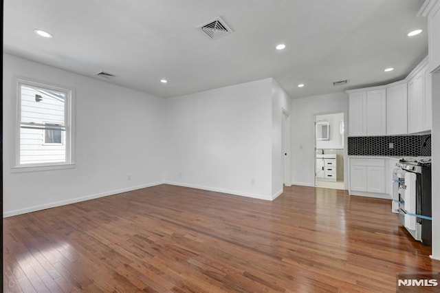 kitchen with hardwood / wood-style flooring, white cabinetry, gas stove, and tasteful backsplash