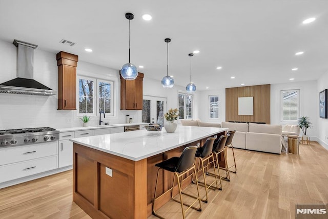 kitchen featuring pendant lighting, stainless steel gas stovetop, a center island, white cabinets, and wall chimney range hood