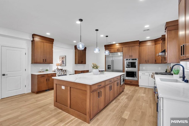 kitchen with light stone counters, sink, built in appliances, decorative light fixtures, and a center island