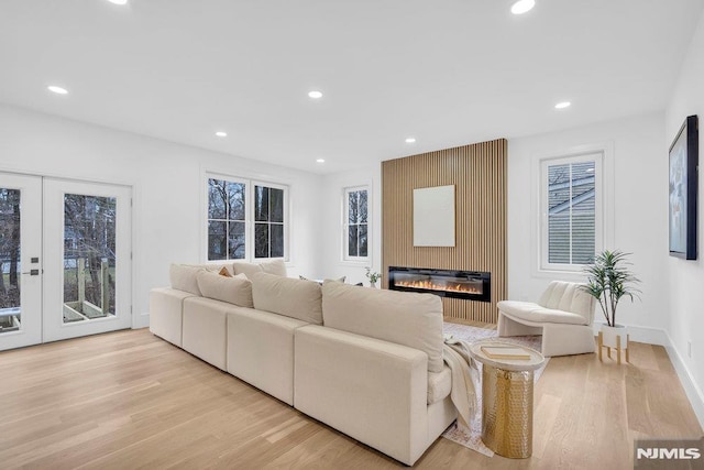 living room with plenty of natural light, a large fireplace, light wood-type flooring, and french doors