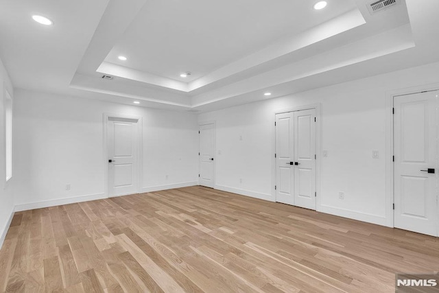 spare room with light wood-type flooring and a tray ceiling