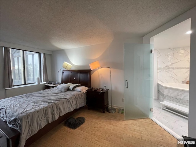 bedroom featuring ensuite bath, light hardwood / wood-style flooring, and a textured ceiling