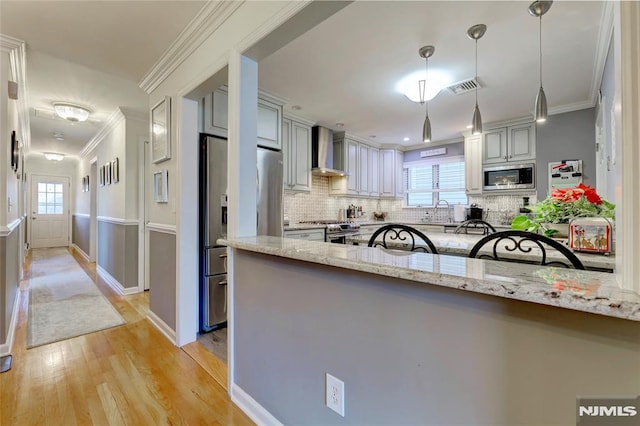 kitchen featuring wall chimney exhaust hood, stainless steel appliances, light stone counters, pendant lighting, and gray cabinets