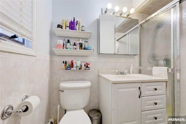 bathroom featuring vanity, a shower with shower door, tile walls, and toilet