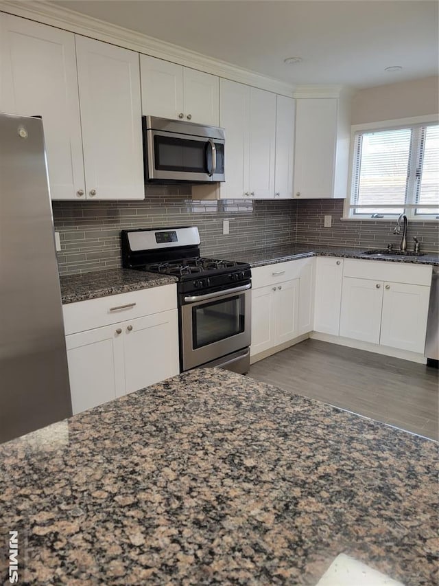 kitchen with white cabinetry, sink, tasteful backsplash, dark stone countertops, and appliances with stainless steel finishes