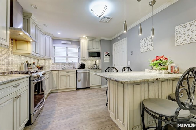 kitchen featuring a breakfast bar area, stainless steel appliances, wall chimney range hood, and cream cabinetry