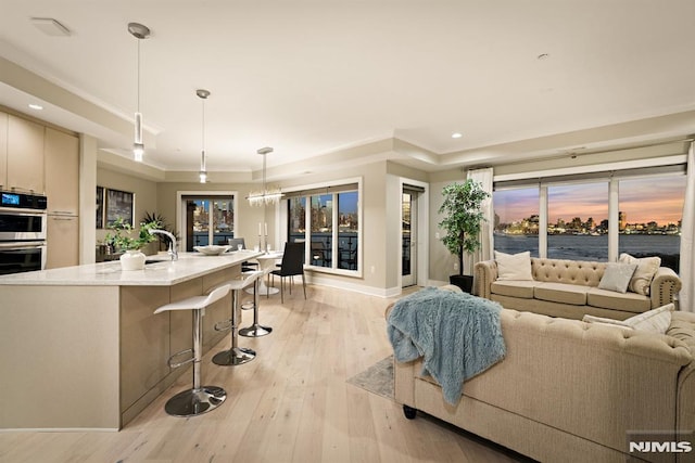 living room with a raised ceiling, light hardwood / wood-style flooring, and an inviting chandelier