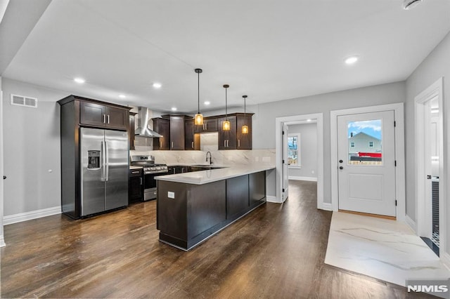 kitchen featuring kitchen peninsula, stainless steel appliances, sink, wall chimney range hood, and hanging light fixtures