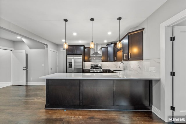 kitchen featuring kitchen peninsula, appliances with stainless steel finishes, decorative light fixtures, and wall chimney range hood