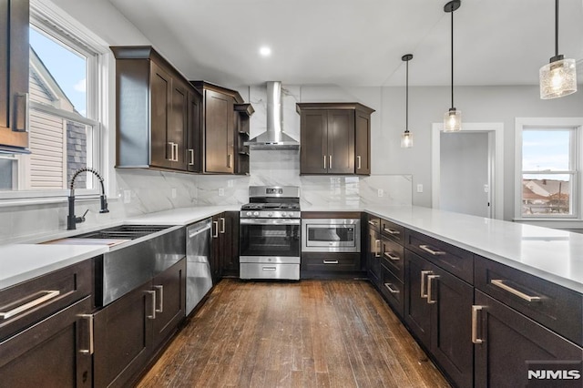 kitchen with wall chimney range hood, hanging light fixtures, decorative backsplash, dark brown cabinets, and stainless steel appliances